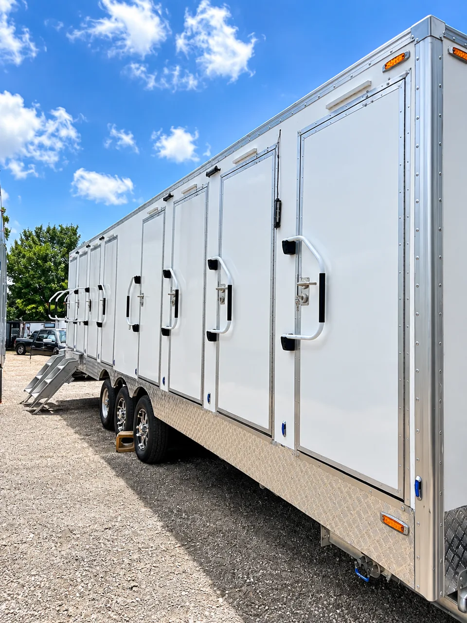 Exterior side view of a 30 ft eight-stall shower and restroom combination trailer parked in an equipment yard with other commercial trailers.